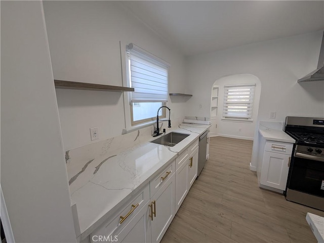 kitchen featuring appliances with stainless steel finishes, white cabinetry, sink, light hardwood / wood-style floors, and light stone countertops