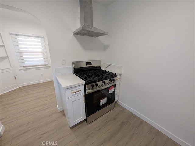 kitchen with white cabinetry, gas range, wall chimney range hood, and light hardwood / wood-style flooring