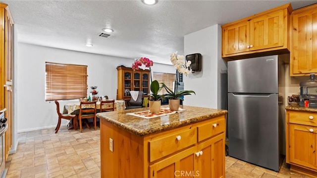 kitchen featuring dark stone counters, stainless steel fridge, and a center island