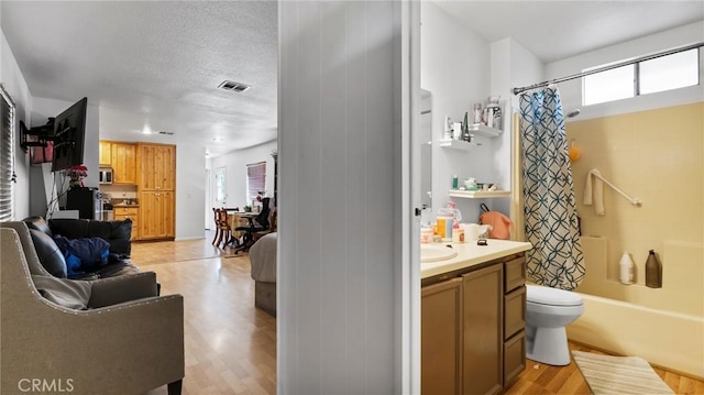 full bathroom featuring shower / bathtub combination with curtain, hardwood / wood-style floors, vanity, a textured ceiling, and toilet