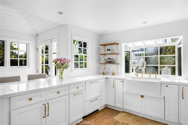 kitchen featuring light wood-type flooring, lofted ceiling, sink, and white cabinets