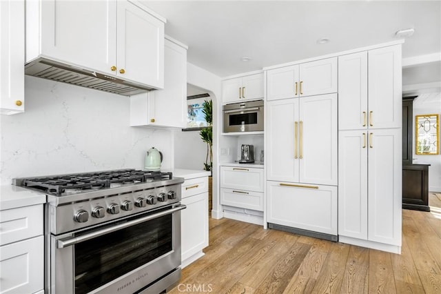 kitchen with stainless steel appliances, decorative backsplash, white cabinets, and light hardwood / wood-style flooring