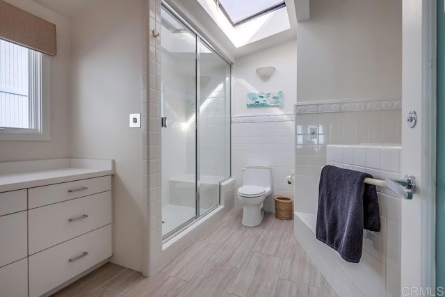 bathroom featuring a skylight, tile walls, vanity, an enclosed shower, and toilet