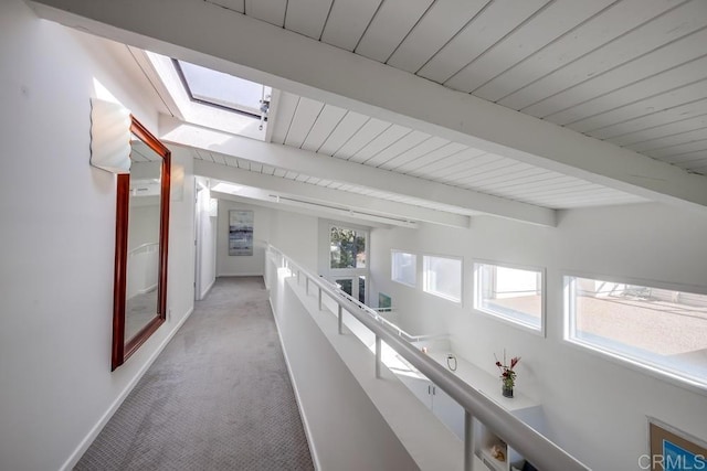 hall with beam ceiling, a skylight, and light carpet