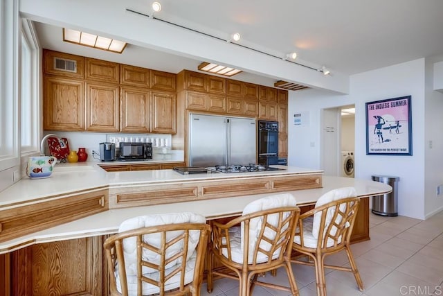 kitchen featuring light tile patterned floors, black appliances, a kitchen bar, washer / dryer, and kitchen peninsula