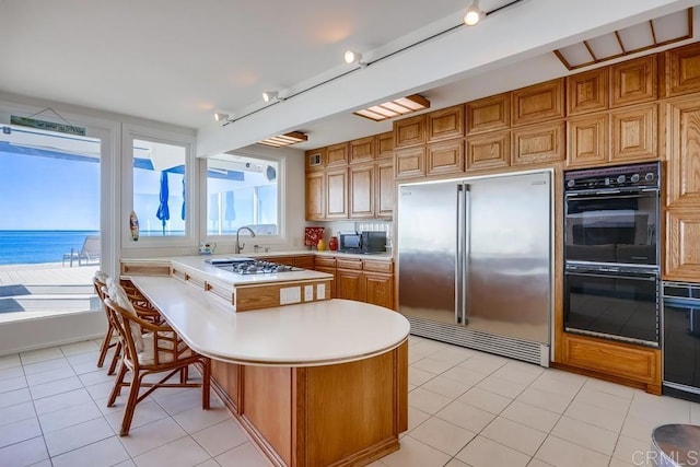 kitchen with light tile patterned floors, a breakfast bar, a center island, a water view, and black appliances