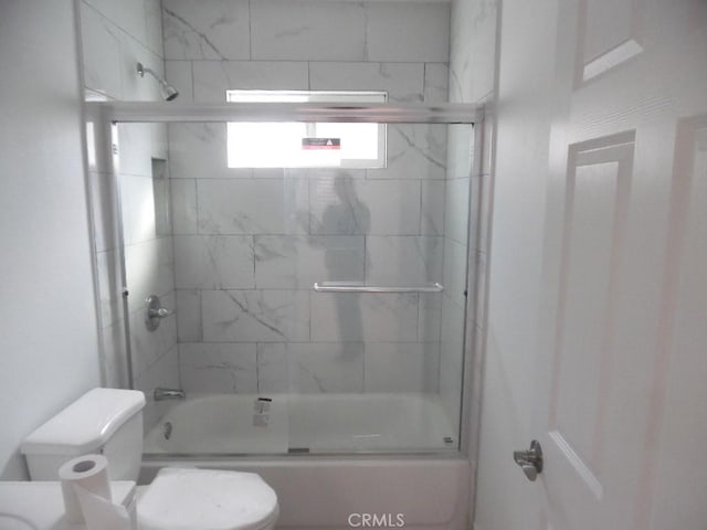 bathroom featuring toilet and bath / shower combo with glass door