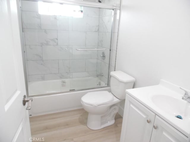 full bathroom featuring vanity, hardwood / wood-style flooring, bath / shower combo with glass door, and toilet