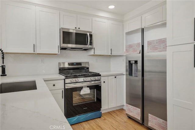 kitchen featuring appliances with stainless steel finishes, white cabinetry, decorative backsplash, light hardwood / wood-style floors, and light stone countertops