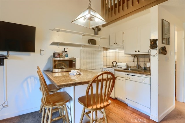 kitchen featuring a kitchen bar, sink, tasteful backsplash, white appliances, and white cabinets