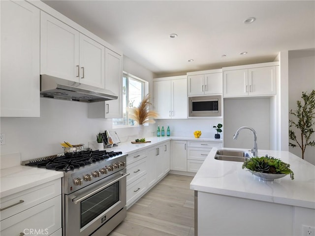 kitchen with sink, white cabinets, light stone counters, stainless steel appliances, and light wood-type flooring