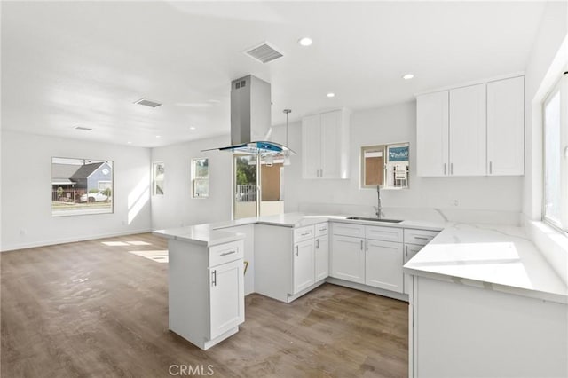 kitchen with sink, hardwood / wood-style flooring, white cabinetry, island range hood, and kitchen peninsula