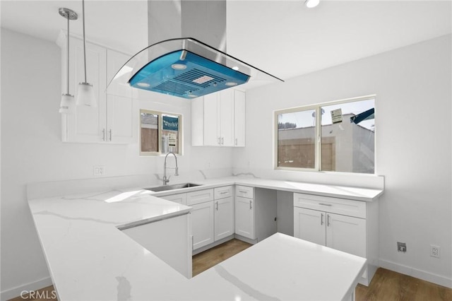 kitchen featuring sink, hanging light fixtures, light stone countertops, white cabinets, and island exhaust hood