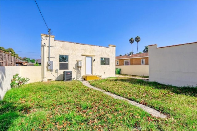 rear view of property with central AC unit and a lawn