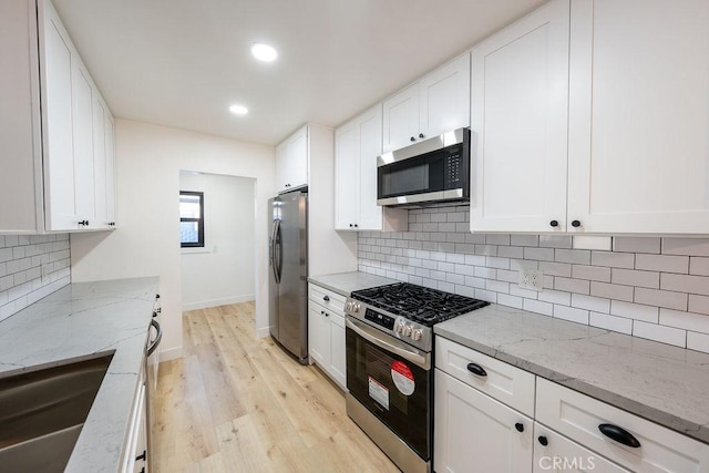 kitchen with tasteful backsplash, light hardwood / wood-style flooring, stainless steel appliances, light stone countertops, and white cabinets