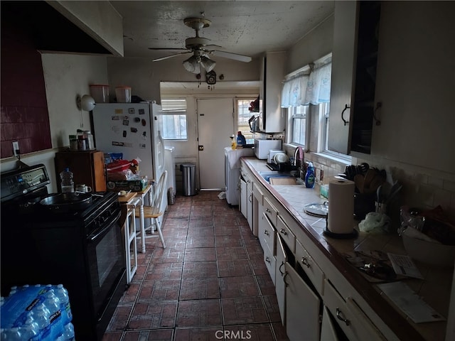 kitchen with sink, ceiling fan, tile counters, white cabinets, and black range