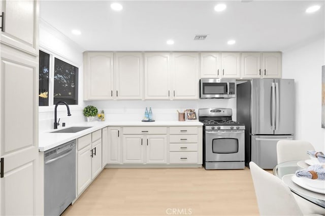 kitchen with stainless steel appliances, sink, white cabinets, and light hardwood / wood-style floors