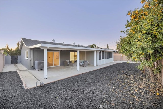 back house at dusk featuring central AC, a sunroom, and a patio