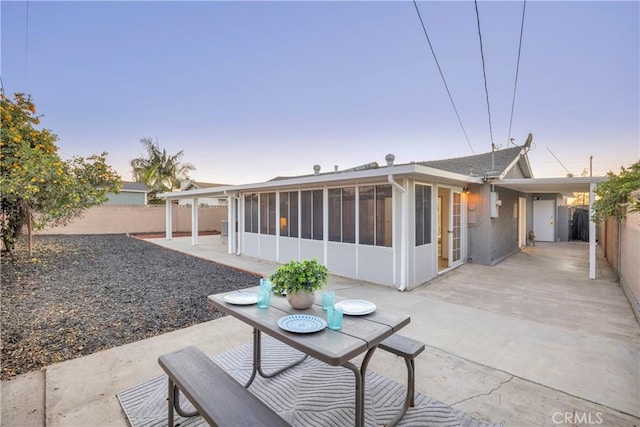 back house at dusk with a sunroom and a patio