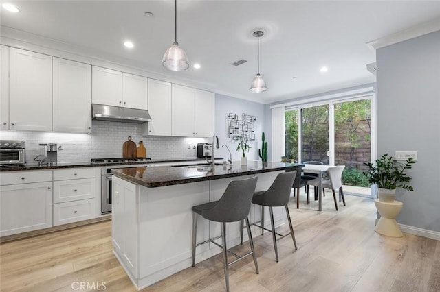 kitchen with white cabinetry, decorative light fixtures, a center island with sink, and stove