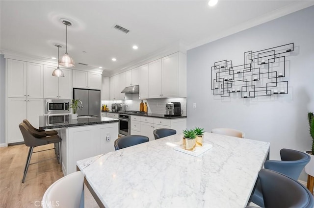 kitchen featuring a breakfast bar area, stainless steel appliances, an island with sink, white cabinets, and decorative light fixtures