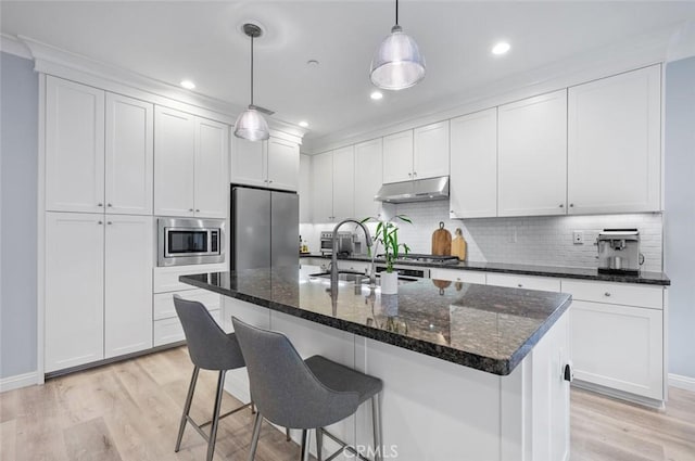 kitchen with decorative light fixtures, white cabinetry, an island with sink, light hardwood / wood-style floors, and stainless steel appliances