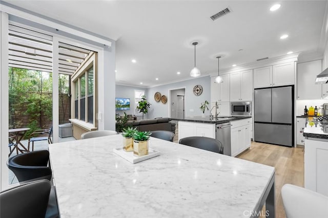 kitchen with appliances with stainless steel finishes, decorative light fixtures, white cabinets, dark stone counters, and a center island with sink