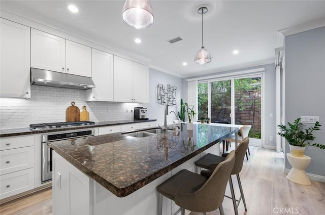 kitchen with an island with sink, appliances with stainless steel finishes, pendant lighting, and dark stone countertops