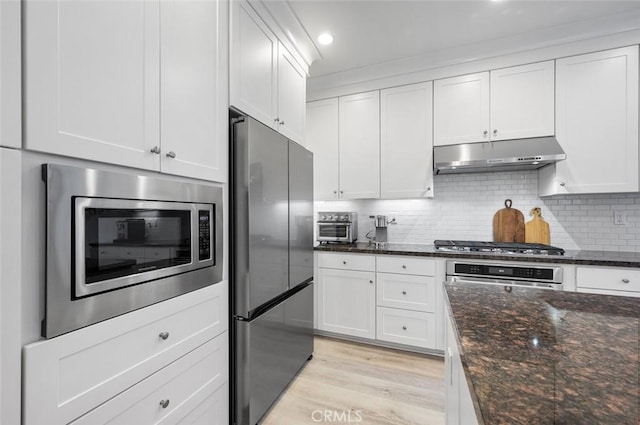 kitchen with decorative backsplash, dark stone counters, white cabinets, and appliances with stainless steel finishes