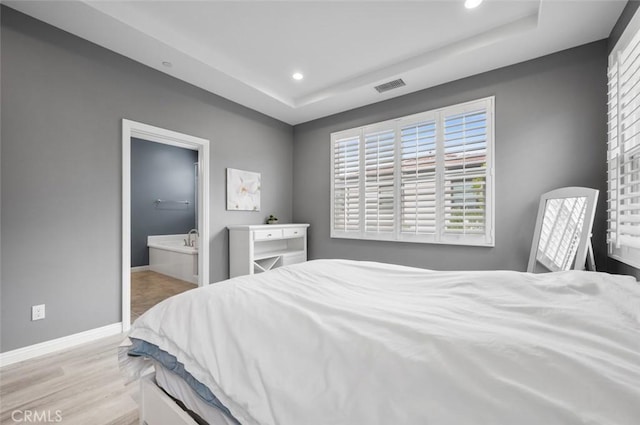 bedroom with light hardwood / wood-style floors, a raised ceiling, and ensuite bathroom