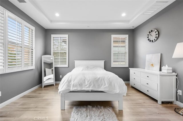 bedroom with light hardwood / wood-style floors and a tray ceiling