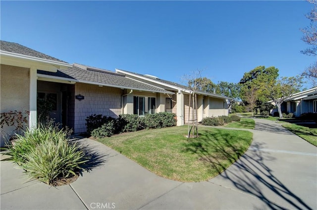 view of front facade with a front yard, roof with shingles, and stucco siding