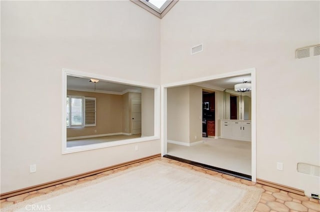 spare room with a skylight, baseboards, visible vents, and a high ceiling