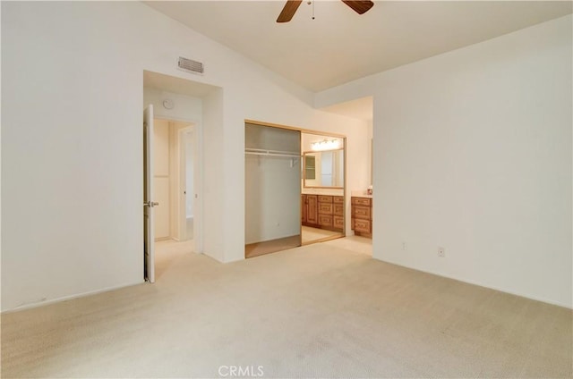 unfurnished bedroom featuring lofted ceiling, light carpet, visible vents, a closet, and ensuite bath