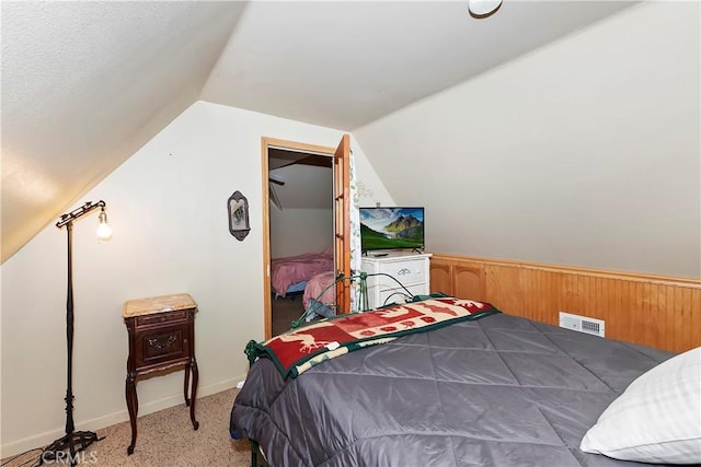 bedroom featuring lofted ceiling, wooden walls, and light colored carpet