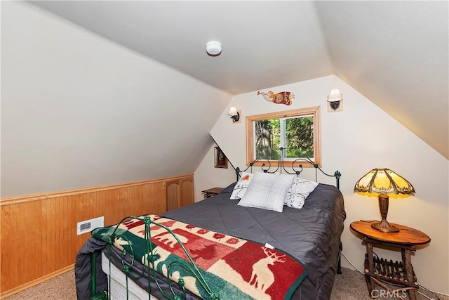 carpeted bedroom with wooden walls and vaulted ceiling