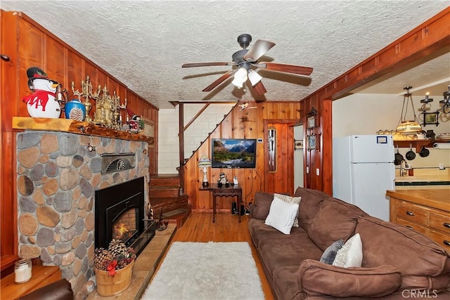 living room with ceiling fan, a fireplace, a textured ceiling, and wood walls