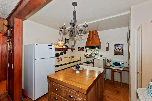 kitchen featuring a kitchen island, pendant lighting, light wood-type flooring, white fridge, and an inviting chandelier