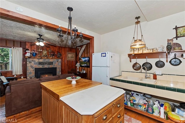 kitchen with sink, ceiling fan, hardwood / wood-style floors, white refrigerator, and a stone fireplace