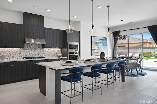 kitchen with decorative backsplash, stainless steel appliances, hanging light fixtures, and a center island with sink