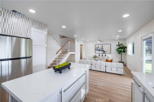 kitchen with stainless steel refrigerator, white cabinetry, a center island, and light stone countertops