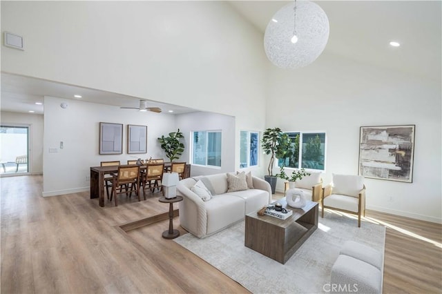 living room with a towering ceiling, ceiling fan, and light hardwood / wood-style flooring