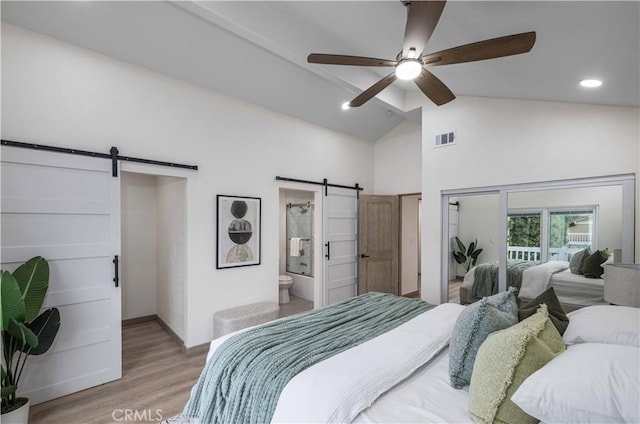 bedroom featuring lofted ceiling, ceiling fan, a barn door, ensuite bath, and light hardwood / wood-style flooring