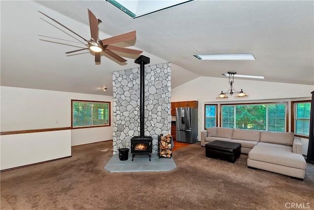 carpeted living room with a healthy amount of sunlight, lofted ceiling, a wood stove, and ceiling fan