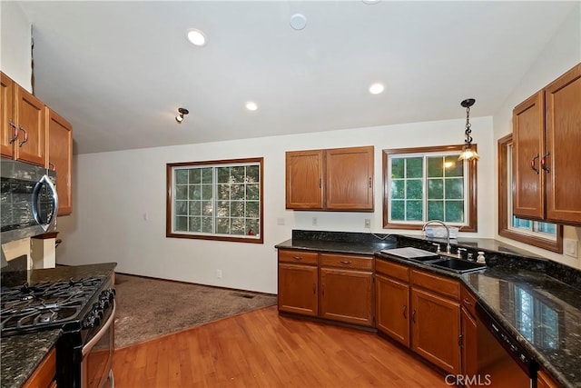 kitchen with sink, light hardwood / wood-style flooring, dark stone counters, pendant lighting, and stainless steel appliances