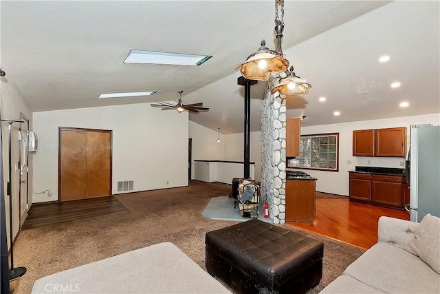 carpeted living room featuring ceiling fan, vaulted ceiling, and a wood stove