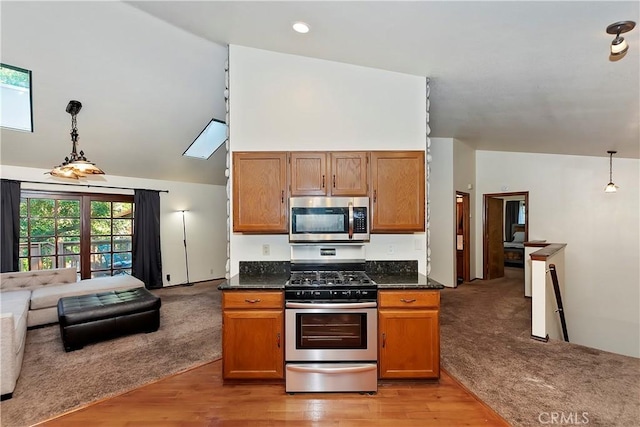 kitchen with appliances with stainless steel finishes, vaulted ceiling with skylight, light carpet, and hanging light fixtures