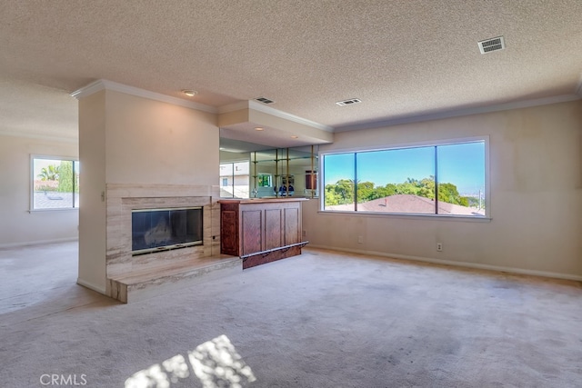 unfurnished living room with ornamental molding, carpet floors, a textured ceiling, and a wealth of natural light