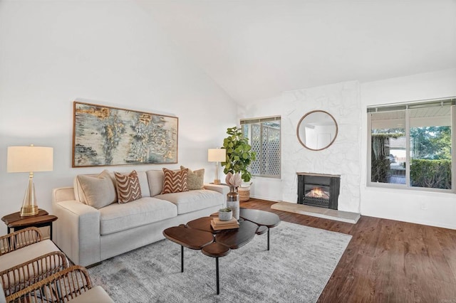 living room with wood-type flooring, a stone fireplace, and high vaulted ceiling