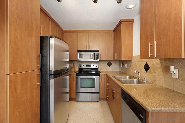 kitchen with light tile patterned flooring, sink, stainless steel appliances, light stone countertops, and backsplash